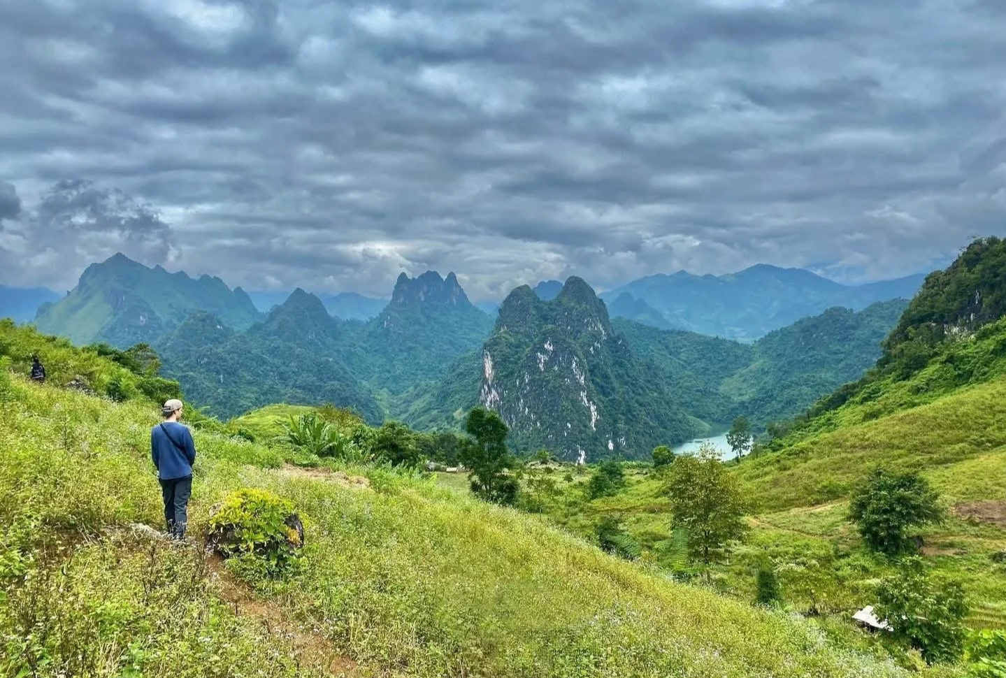 A person standing on a grassy ridge looking out over dramatic mountain peaks in Dien Bien Phu region.