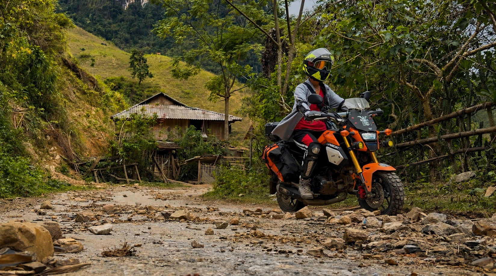 Motorbike rider crossing mixed road conditions in Lai Chau Province including rocks, dirt, and uneven surfaces in northern Vietnam