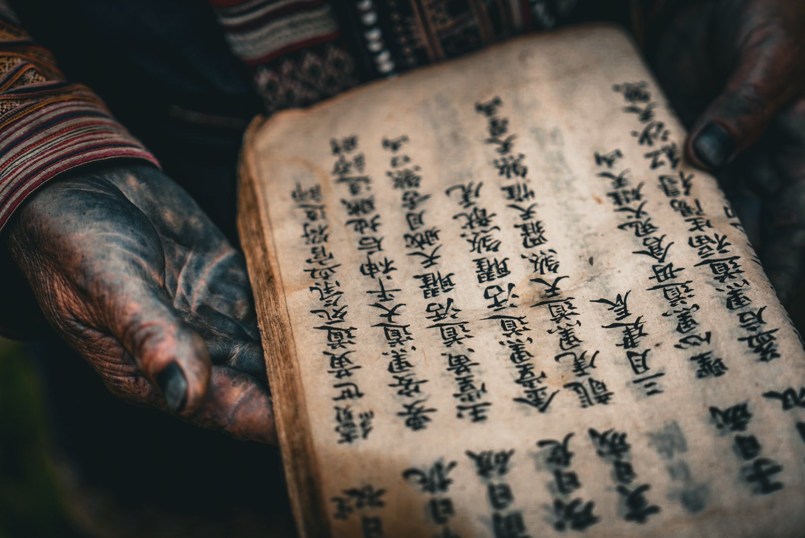Indigo-stained hands of a Red Dao (Iu Mien) woman holding a handwritten ritual manuscript on traditional handmade paper in Sa Pa, Vietnam.