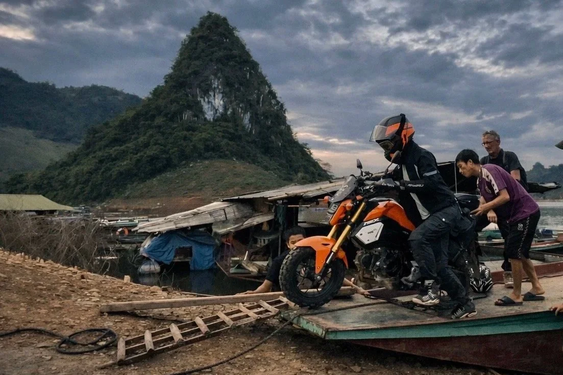 Motorbikes being transported across a lake on a small boat during a journey through the mountains of northern Vietnam.