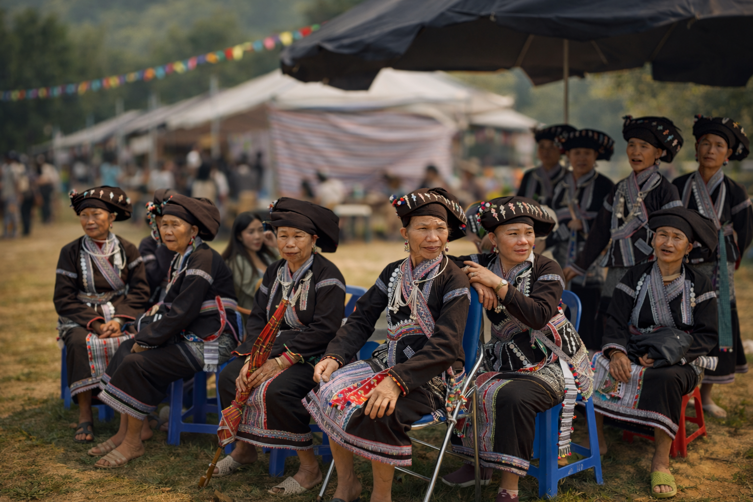 Lao women seated together in traditional embroidered clothing and headdresses, watching the festival unfold in Lai Châu, their expressions warm and attentive as community life gathers around them.