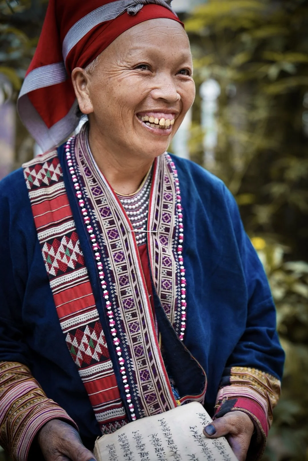 Red Dao (Iu Mien) woman in Sa Pa holding a handwritten family ritual manuscript on traditional handmade paper.