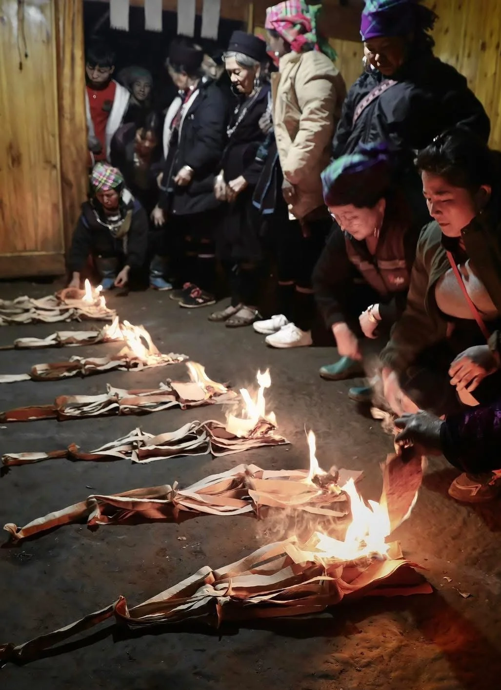 Long rows of rolled paper offerings burn on the floor as women observe during a Hmong ceremony.