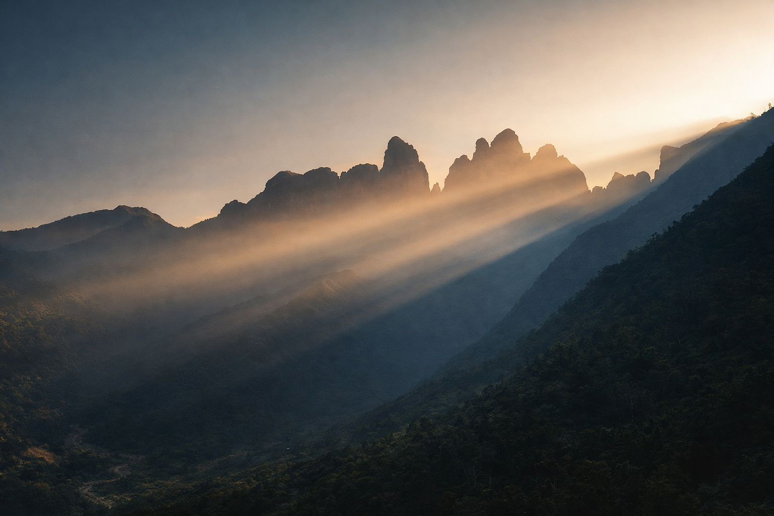 Golden sunlight breaking through mountain peaks, casting long rays across layered ridgelines at sunrise or sunset.
