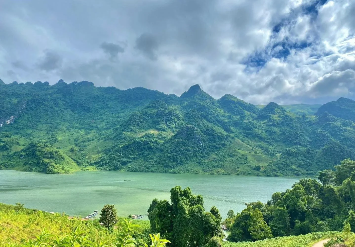 A wide view of mountains surrounding a calm lake in Dien Bien Phu under phuunder dramatic cloudy skies.