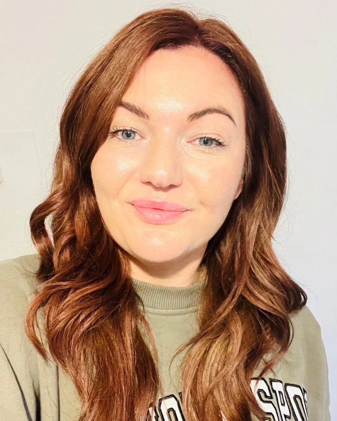 A woman with shoulder-length red hair and blue eyes smiling, wearing a green sweatshirt.