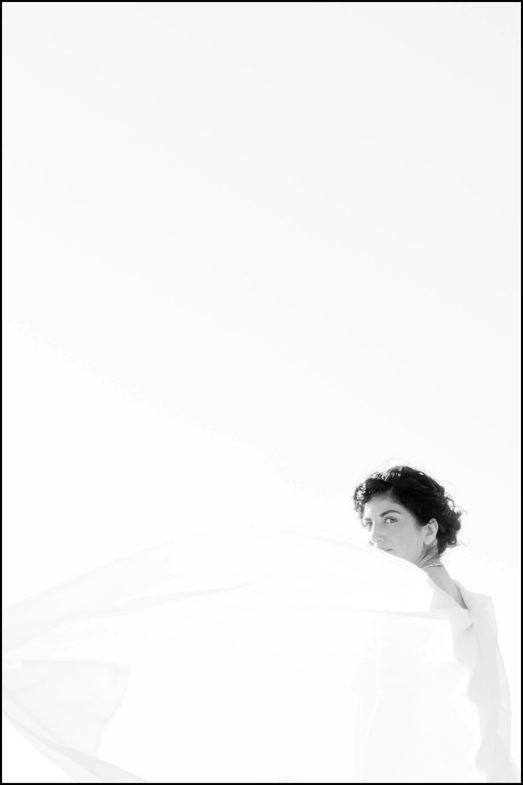 Black and white portrait of a woman with dark curly hair, resting her chin on her arm and gazing at the camera, set against a plain white background.