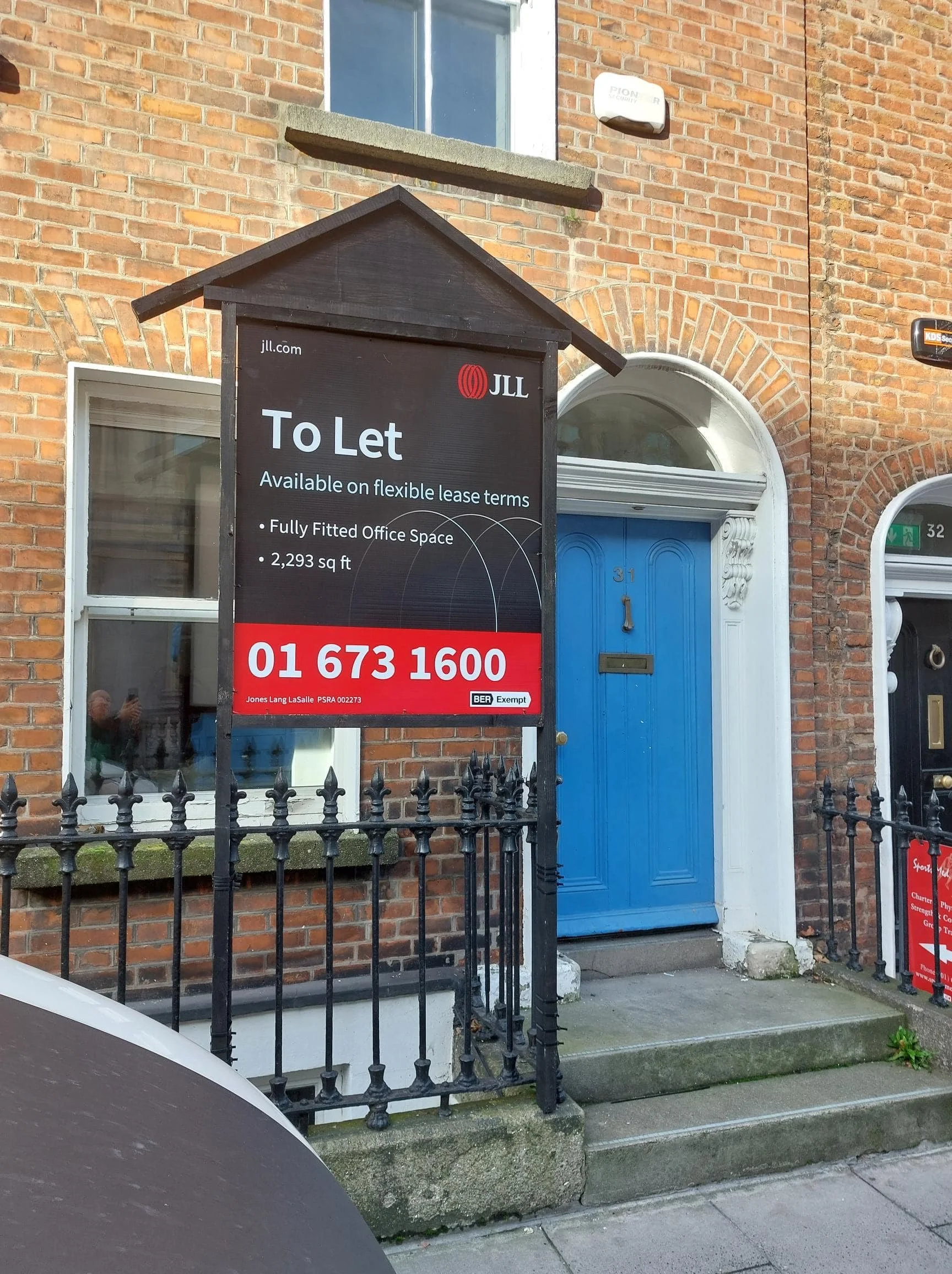A real estate sign advertising a fully fitted office space available for lease at 31 Jones Lang LaSalle PSRA 002273 with contact number 01 673 1600, located outside a building with a bright blue door, white trim, brick exterior, and a small porch with steps.