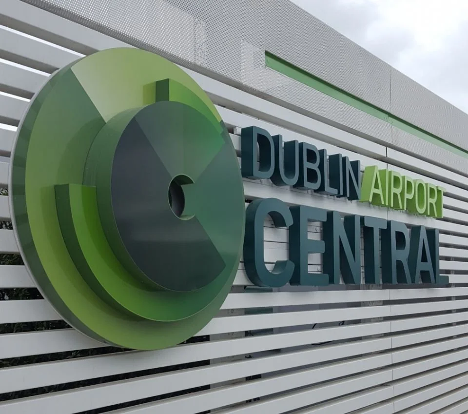 Sign for Dublin Airport Central with a green and black logo on a white slatted wall.