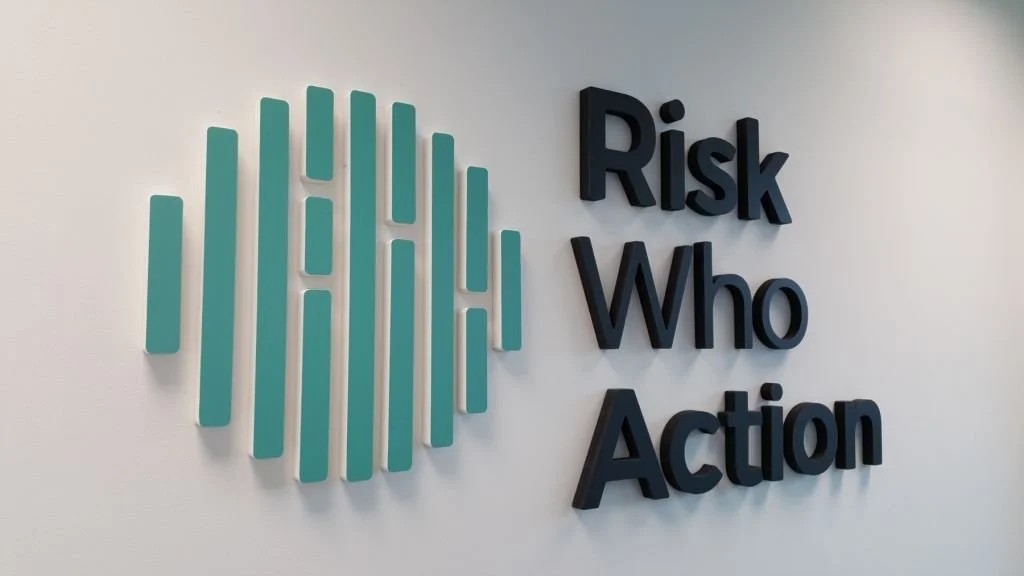 Office wall with the words "Risk Who Action" displayed in large black 3D letters and a teal circular logo made of vertical lines.