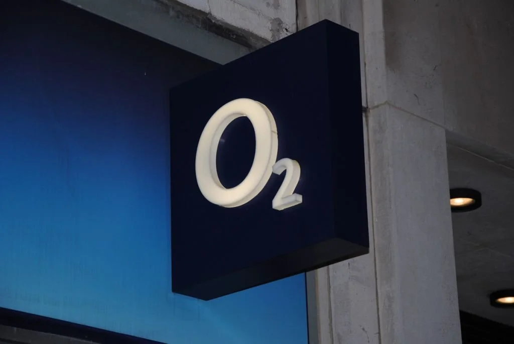 A black square sign with the white illuminated text 'O2' attached to a concrete wall.