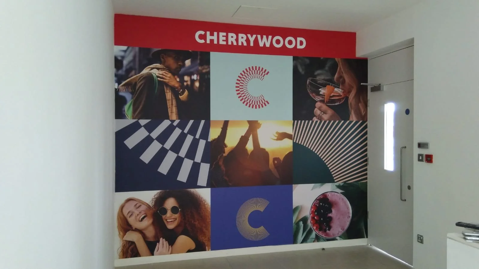 A colorful wall mural with the word 'CHERRYWOOD' at the top, featuring images of people enjoying various activities, abstract designs, and a glass of pink drink, in a modern indoor setting.