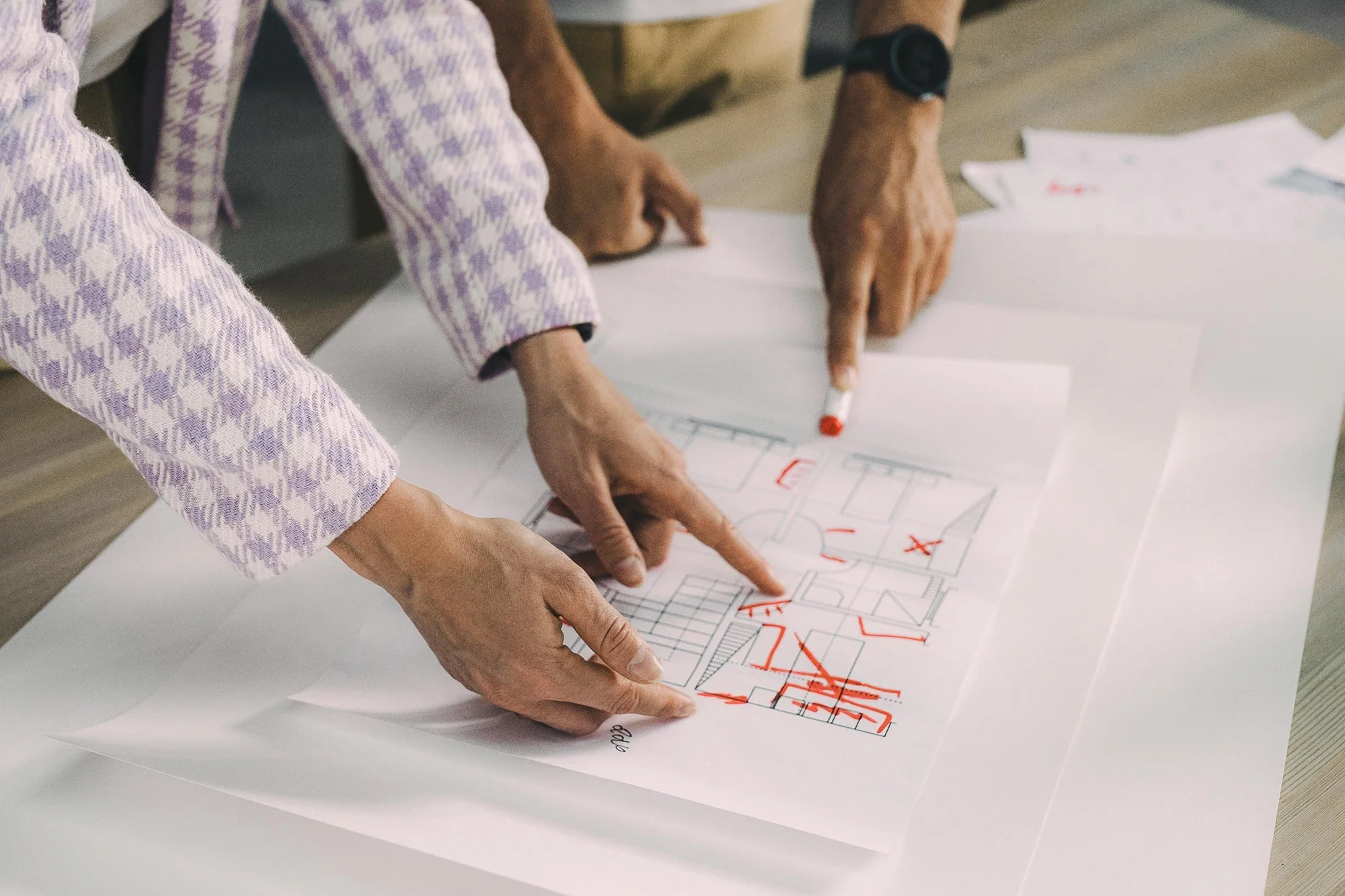 Two people reviewing architectural blueprints on a table, with one pointing at a section marked in red.