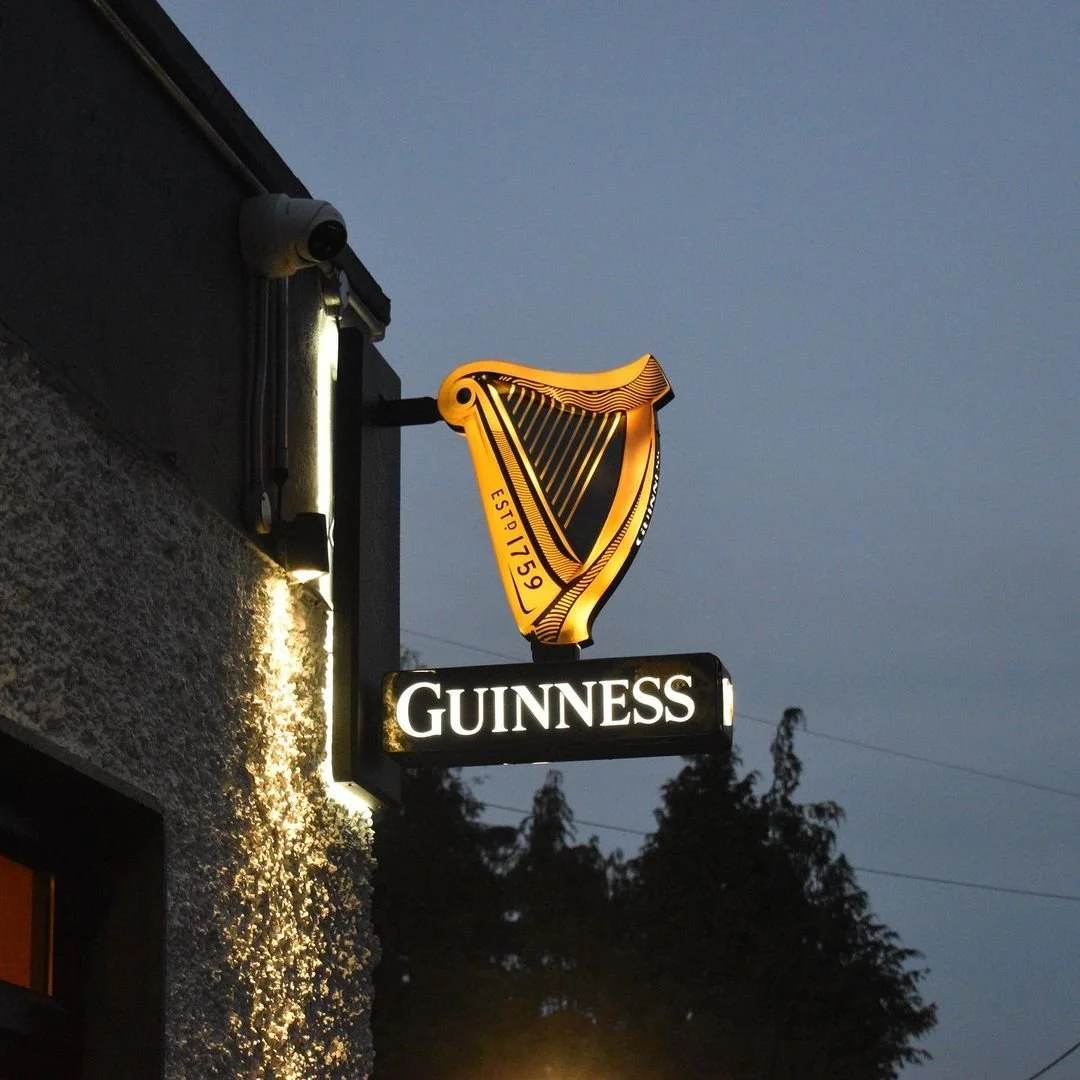 A neon sign displaying a harp and the name "Guinness" on a building at dusk.