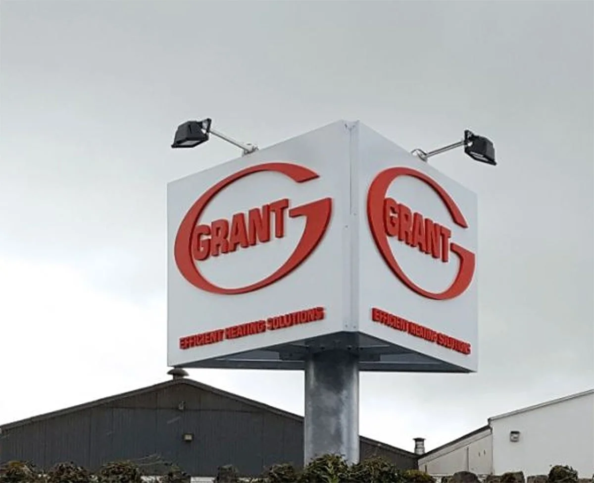 A large billboard with red and white branding for Grant, emphasizing efficient heating solutions, mounted on a tall pole against a cloudy sky.