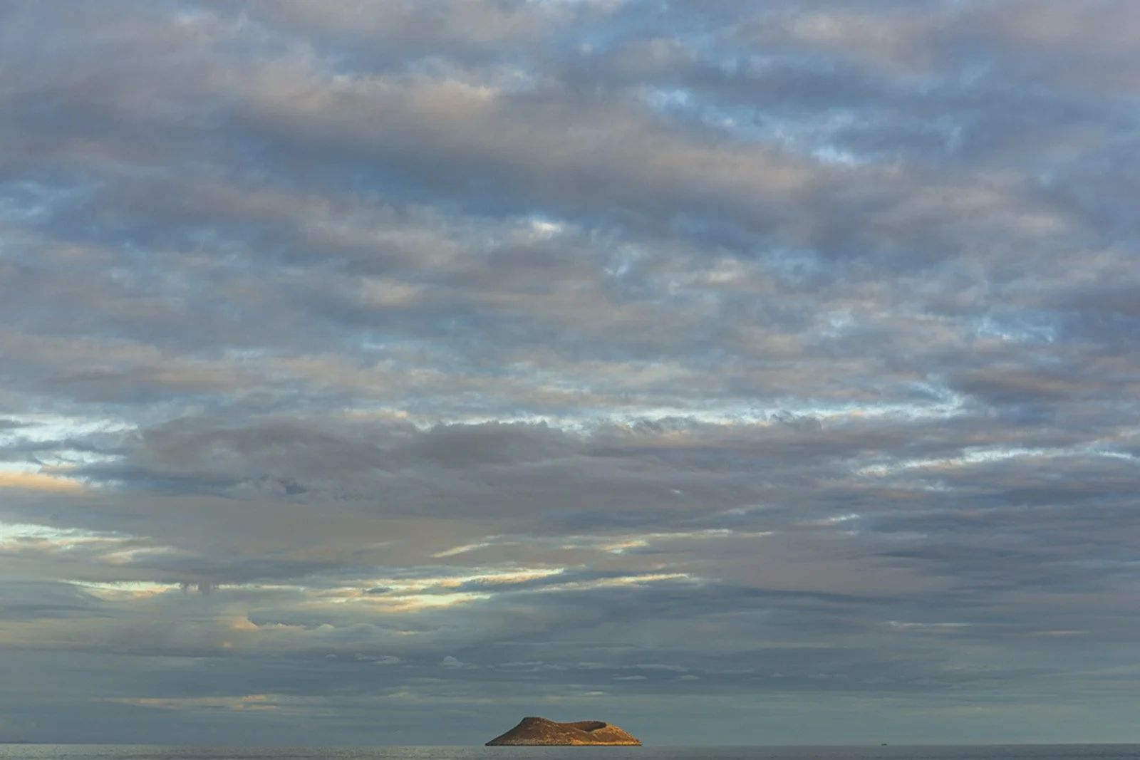 A small island surrounded by ocean beneath a partly cloudy sky.