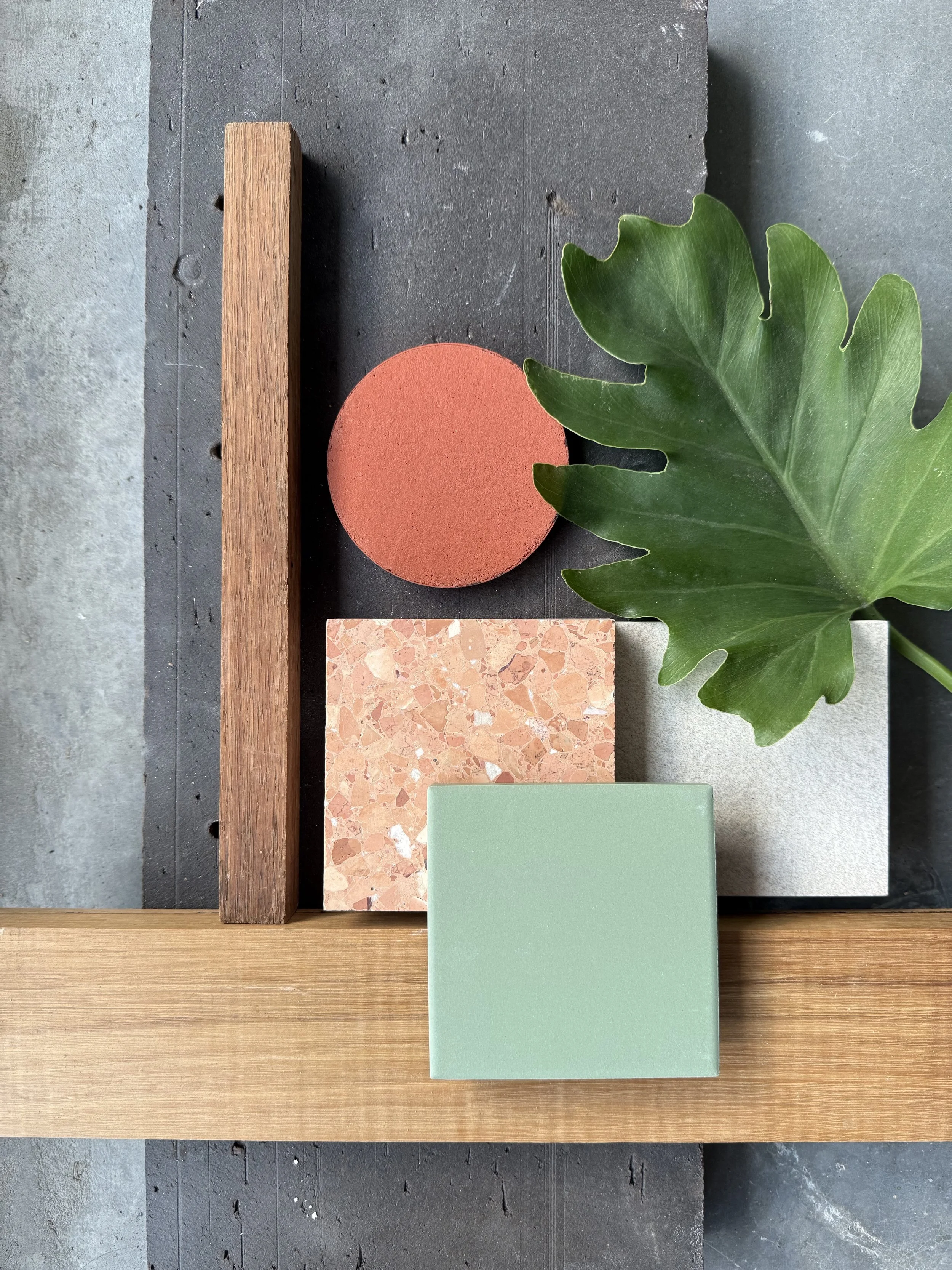 Flat lay image with green tile, orange terrazzo and timber samples on concrete background.