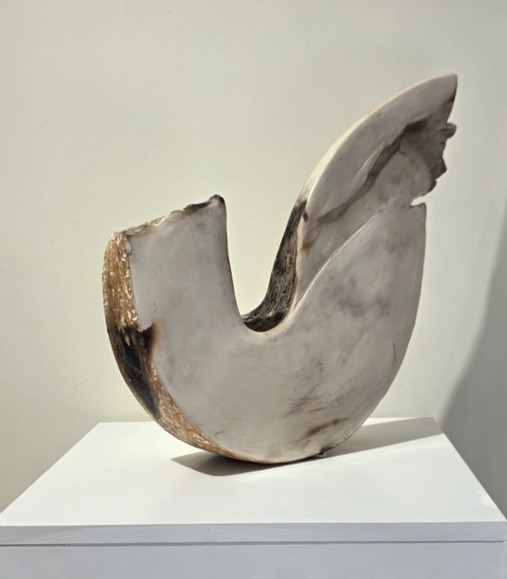 Statue abstraite en pierre ou en marbre blanc, ressemblant à une forme incurvée ou un croissant, placée sur une plateforme blanche.