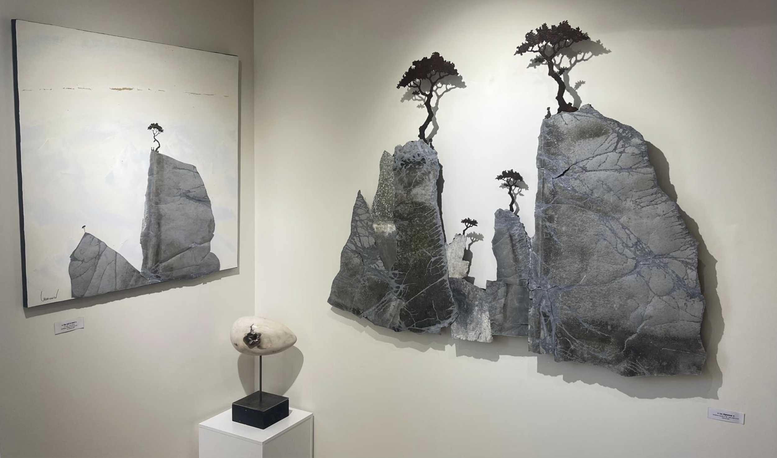 Une œuvre d'art constituée de plusieurs roches plates et de petits arbres stylisés, avec une peinture représentant également des roches et des arbres en arrière-plan.