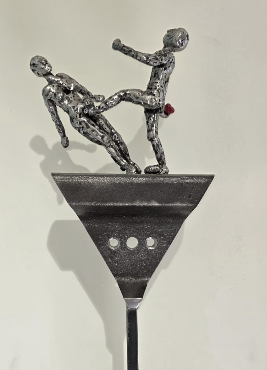 Une sculpture representing deux hommes, l'un en train de faire un saut et l'autre en position de réception. La sculpture est en métal et installée sur un support en forme de cône.