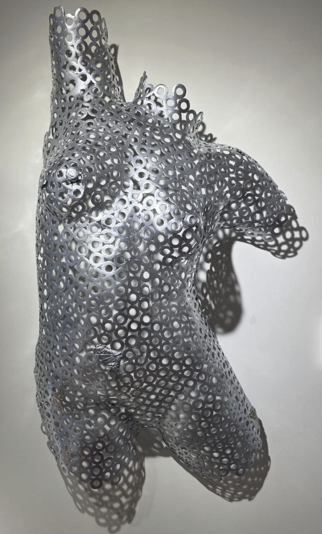 Sculpture de femme en métal perforé représentant une femme stylisée, vue de face, avec un fond neutre.