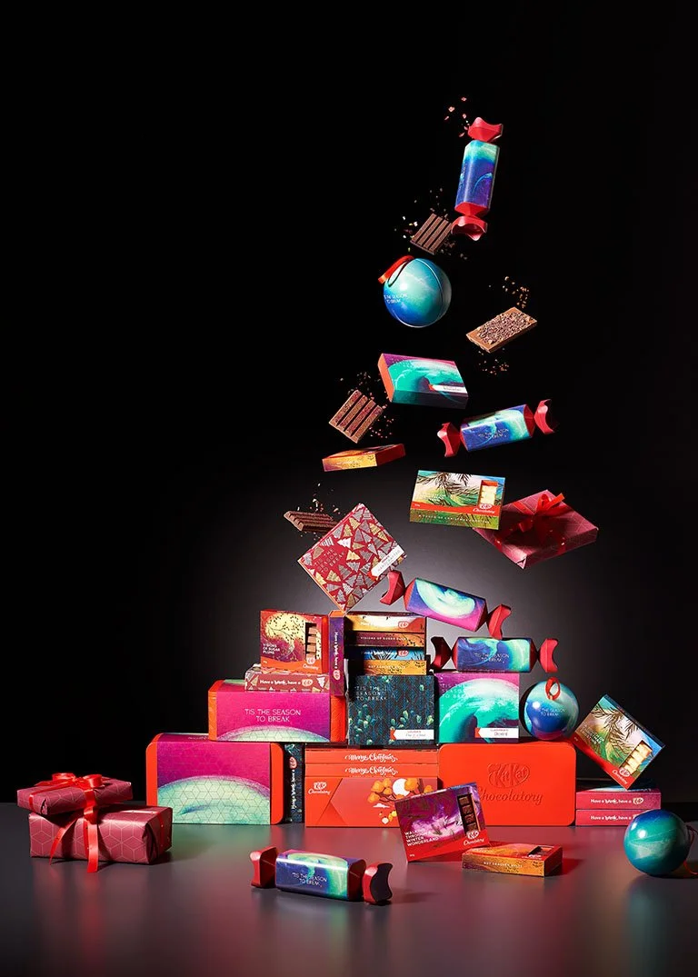 Christmas-themed assorted chocolates and candy boxes arranged in a shape resembling a Christmas tree against a black background.