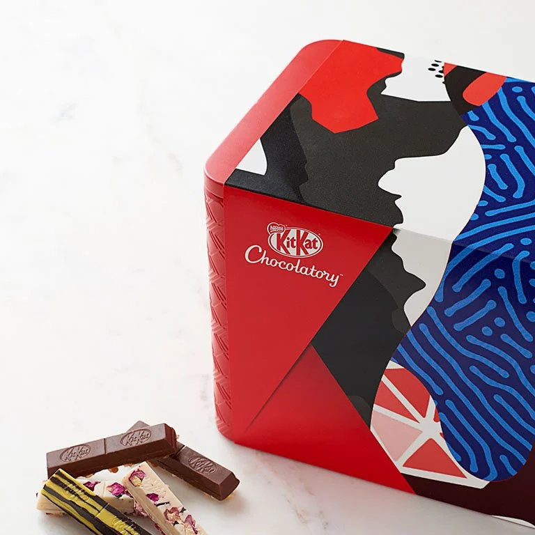 Red Kit Kat Chocolatory limited edition box with geometric and abstract design, featuring a stylized face and fingerprint pattern, with some chocolate pieces placed in front.