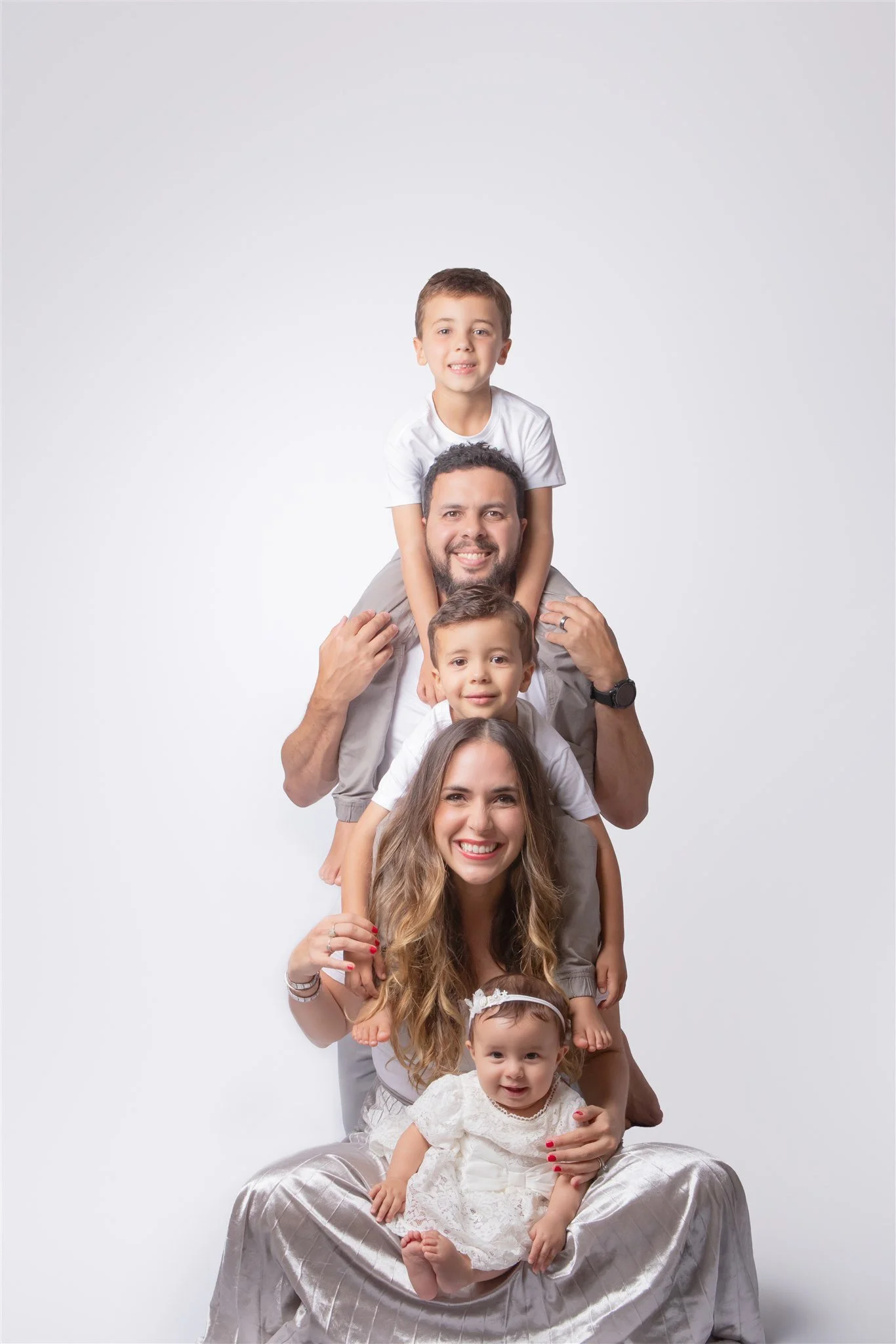 A family of six, including two parents and four children, stacked in a vertical line, smiling, against a plain white background.