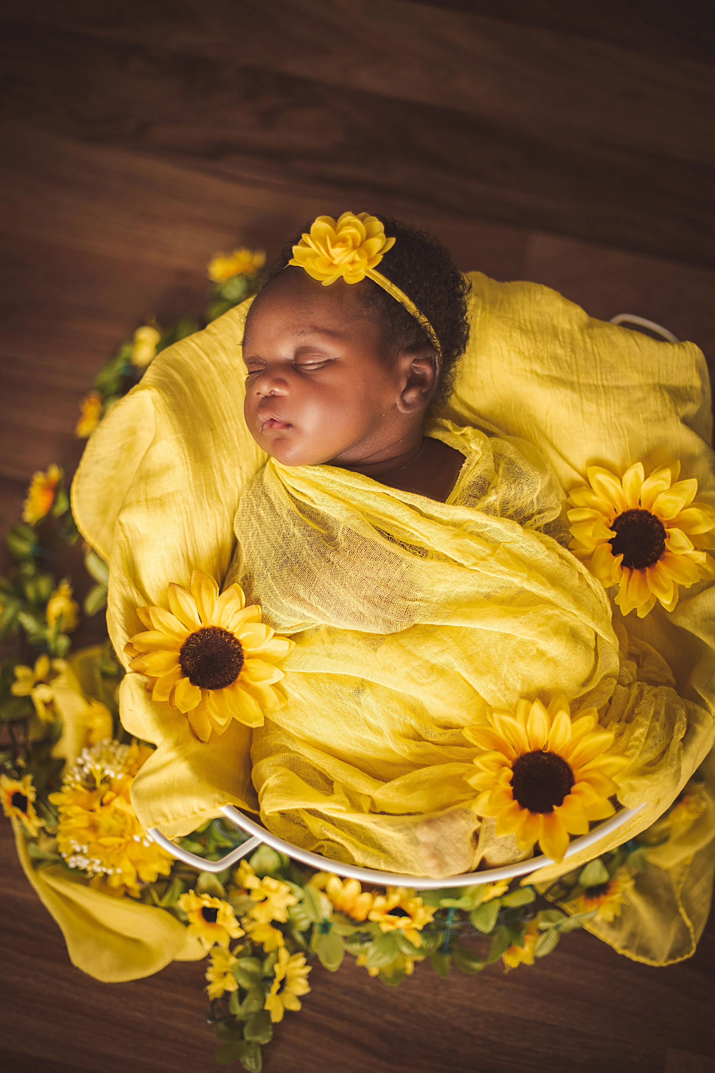 A sleeping baby girl wrapped in yellow cloth and surrounded by yellow flowers.