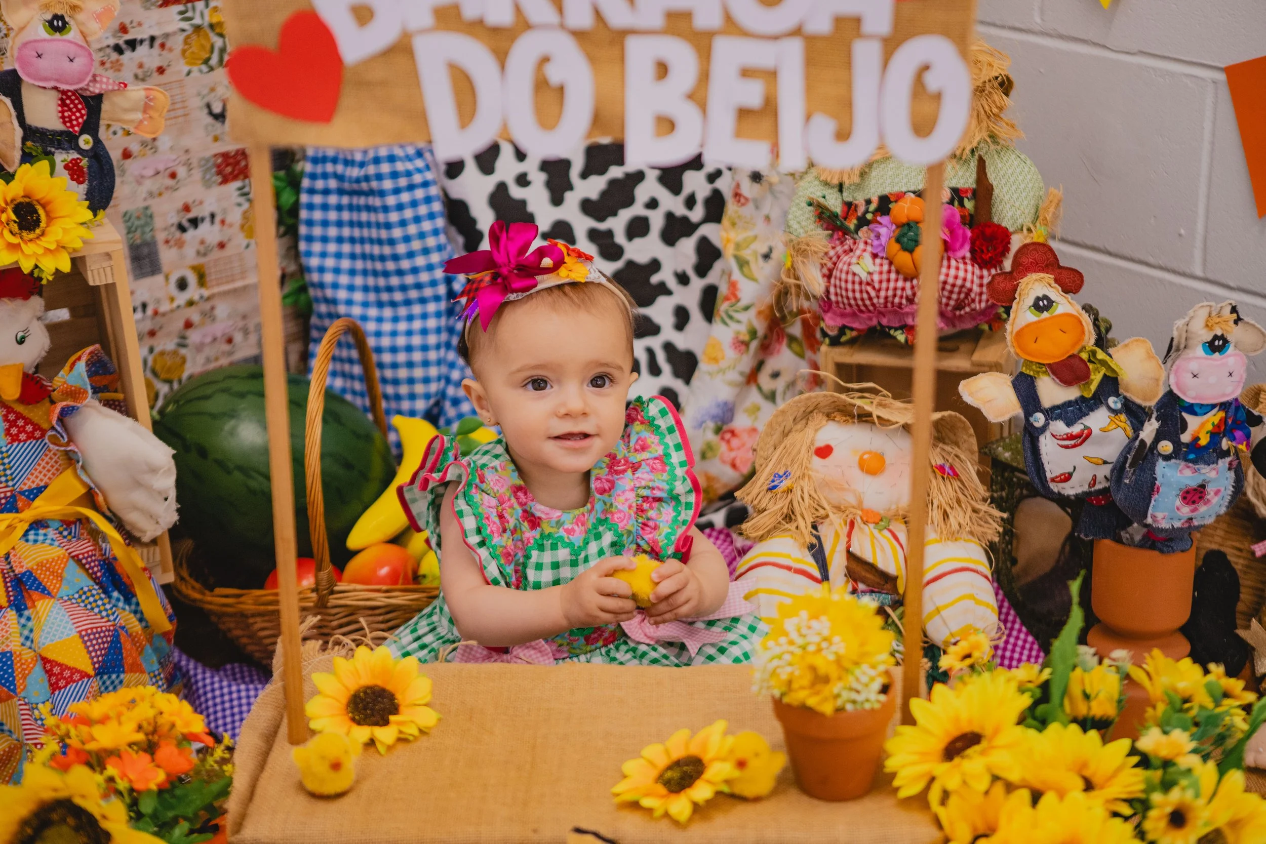 A young girl sitting at a decorated table with sunflowers, holding a small yellow chick figurine, surrounded by colorful plush dolls and seasonal decorations for a celebration.