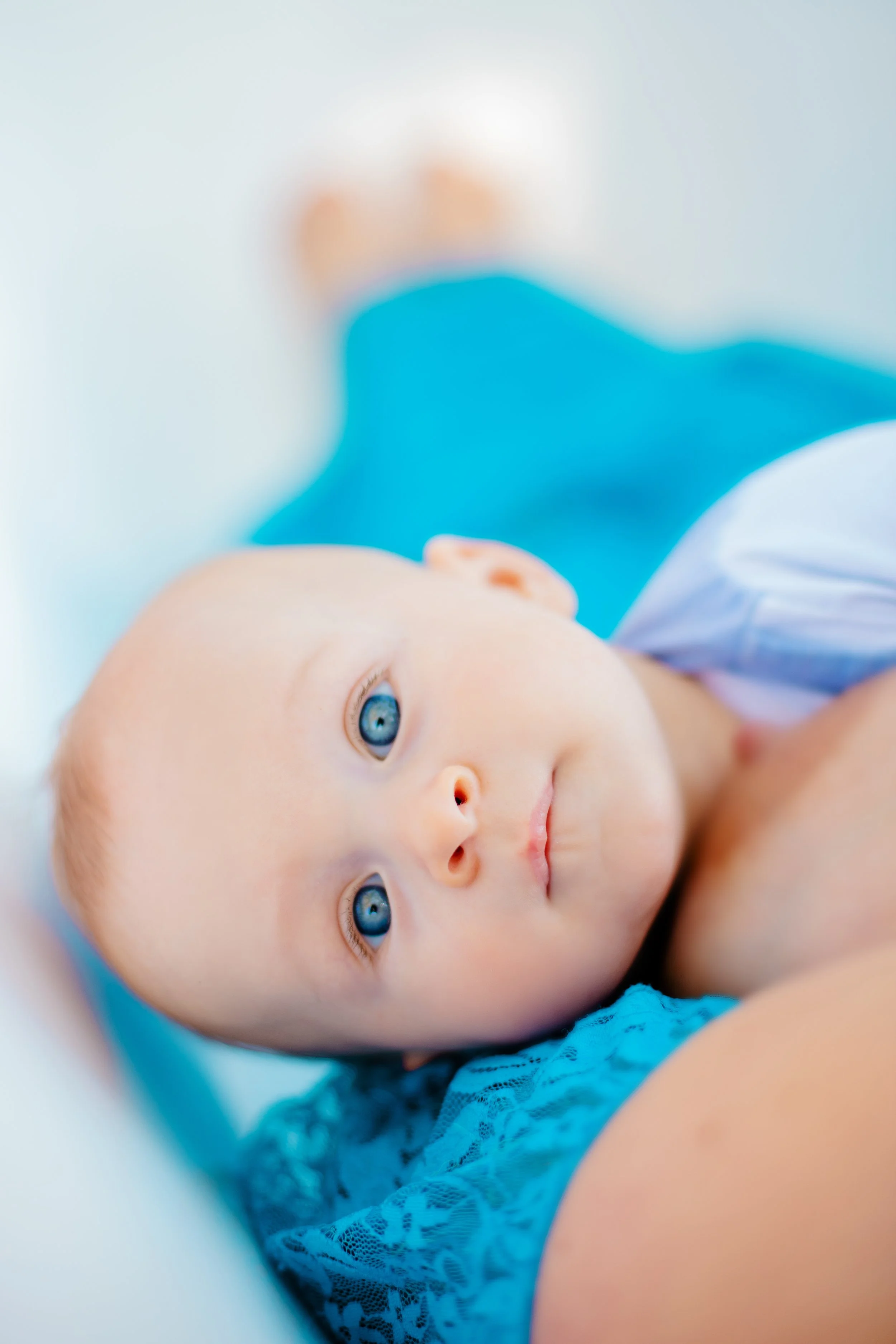 A close-up of a young child with blue eyes lying on an adult's chest, looking up, with a blurred background and the adult wearing a blue shirt.