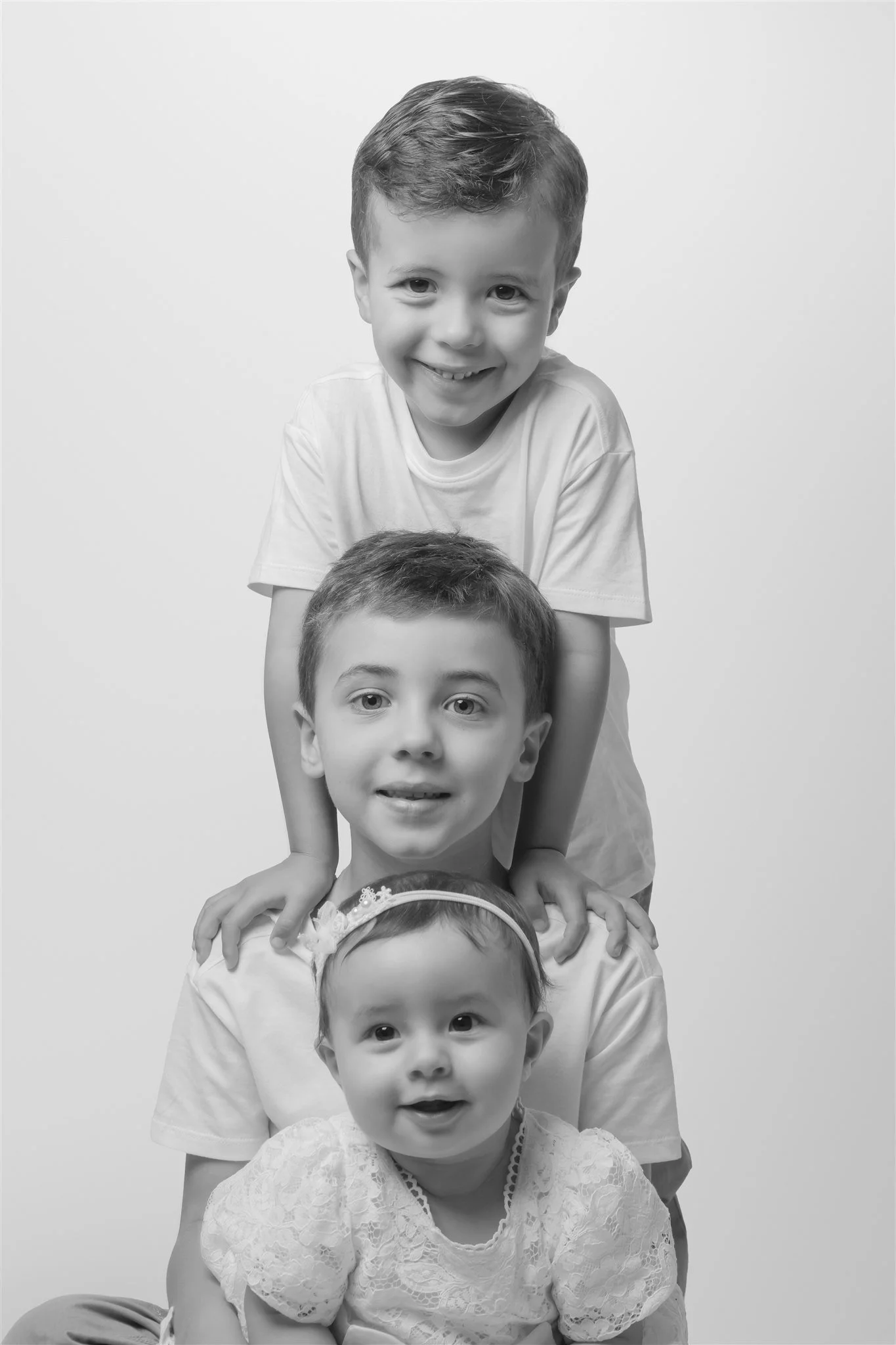 Four children stacked in a line, smiling, black and white photo.