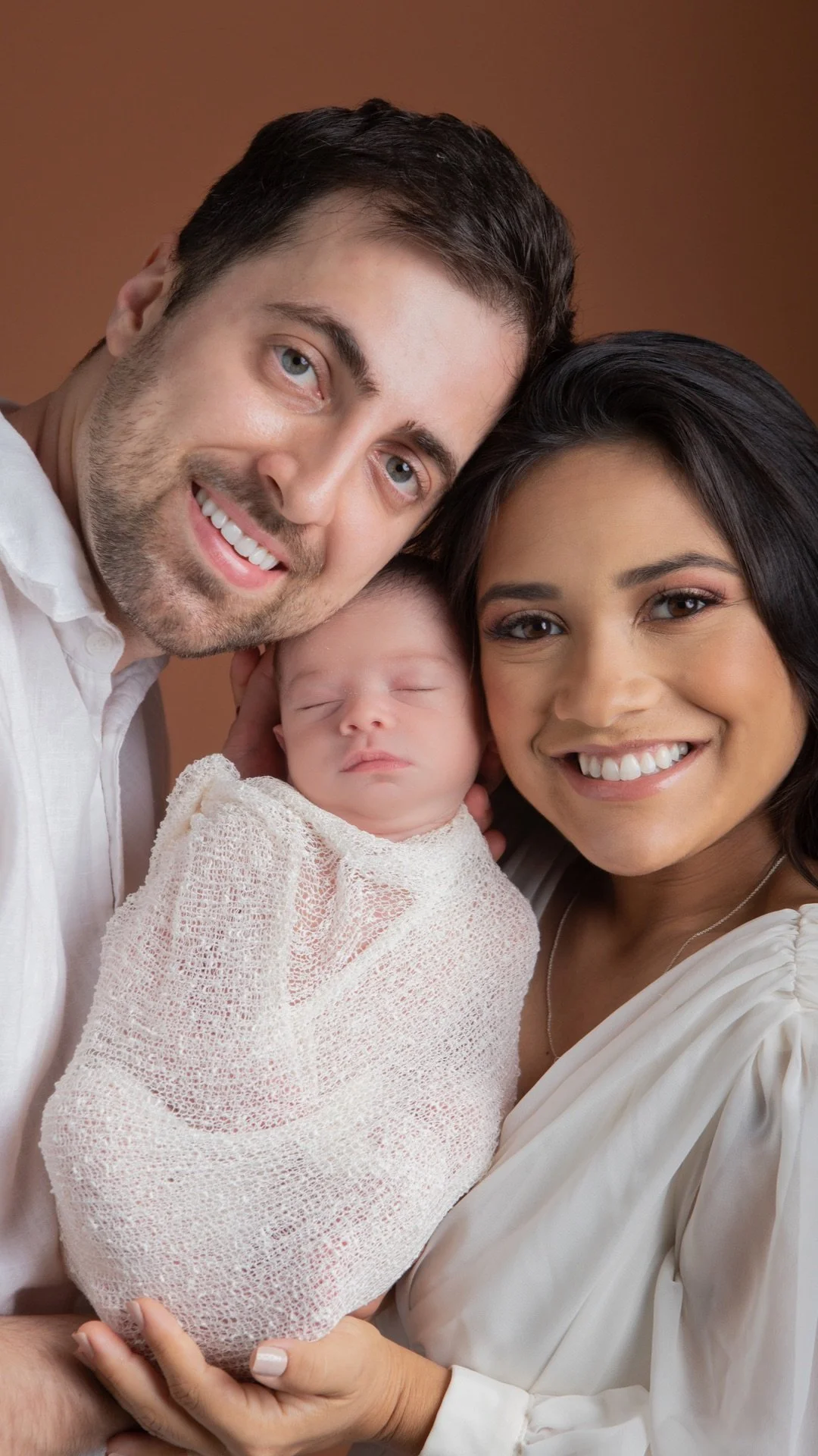 A happy family of three, a man, woman, and baby, smiling and posing for a photo.