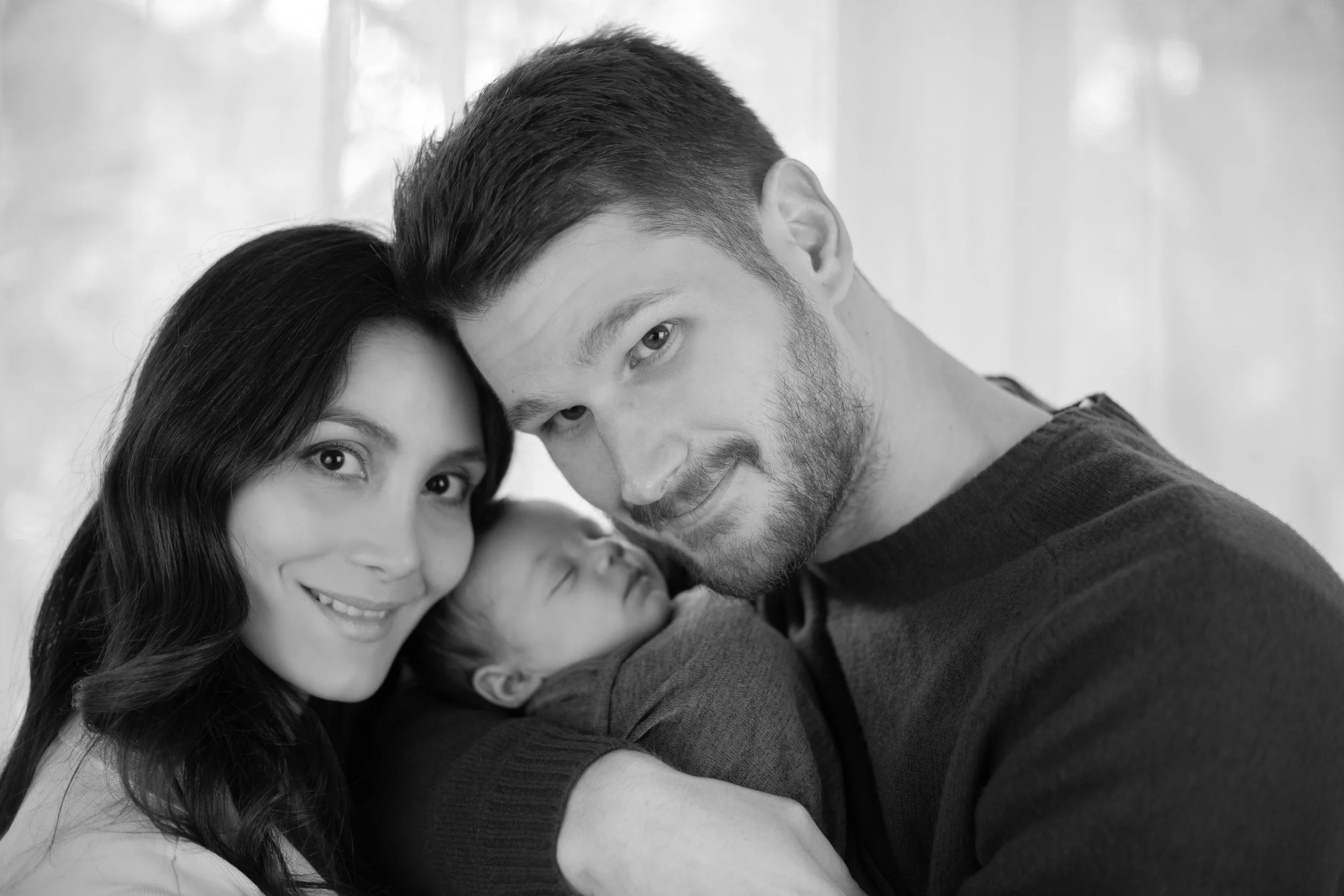 A family of three with a woman, a man, and a newborn baby in a close-up portrait, black and white photograph.