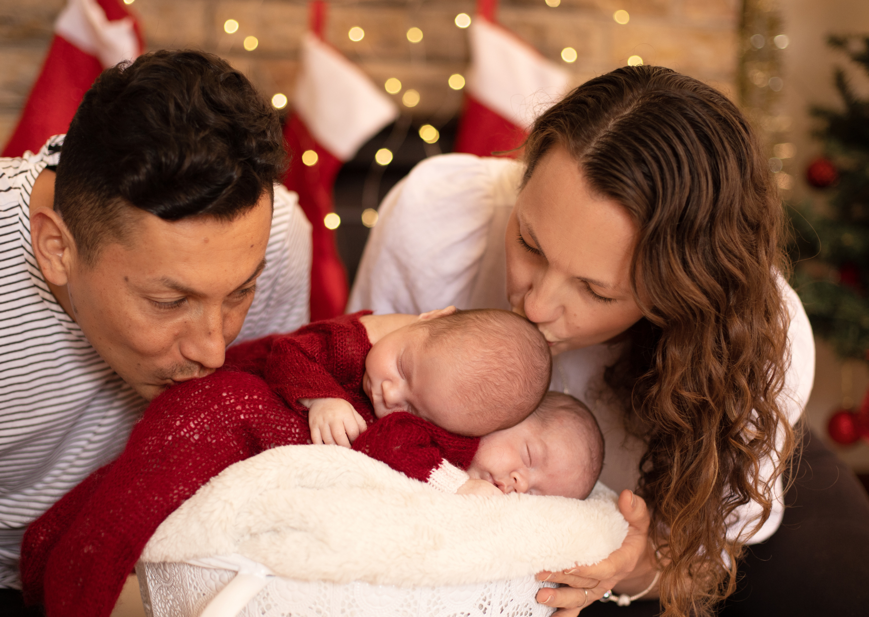 Family celebrating Christmas with two newborns, decorating stockings and Christmas tree in the background.