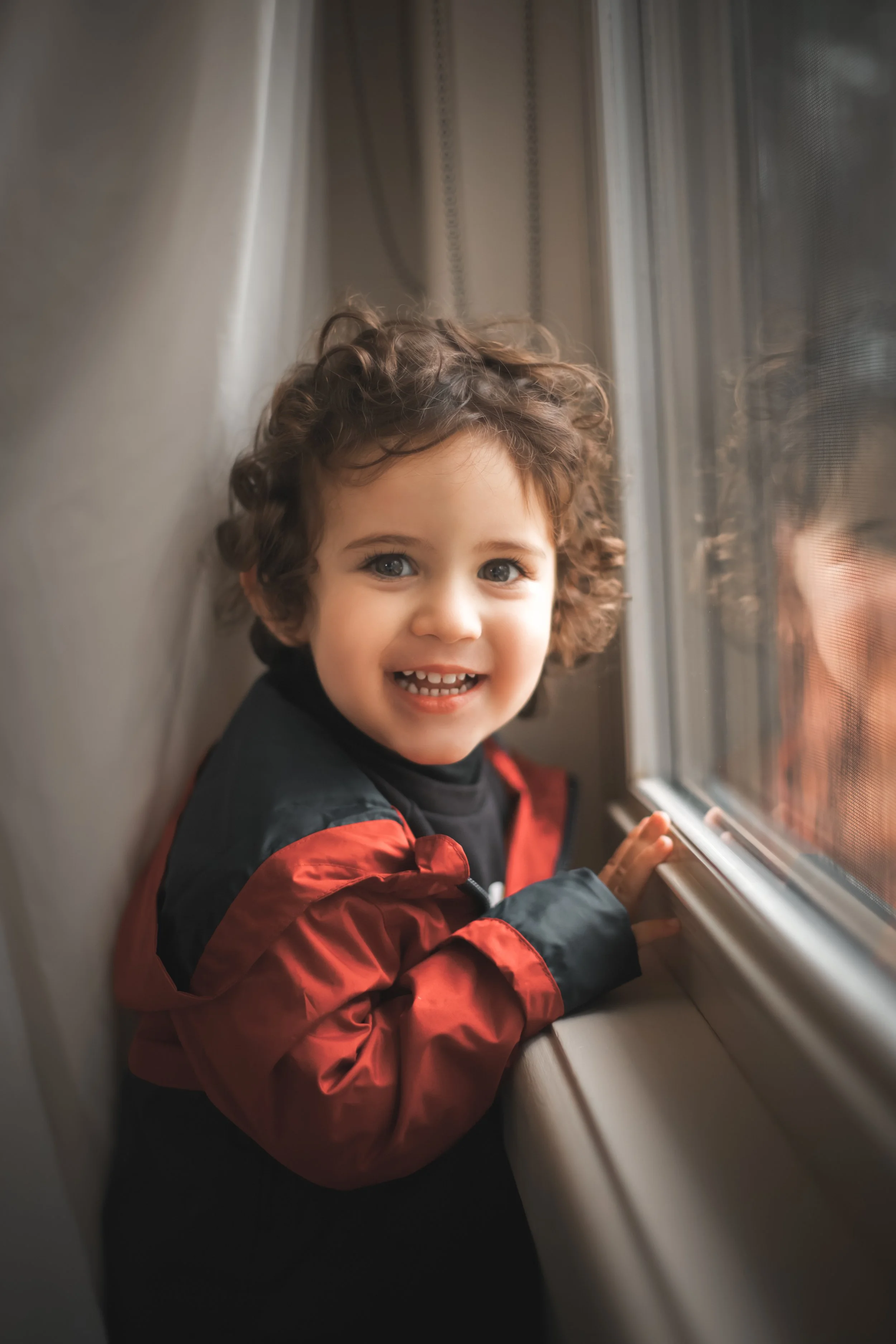 Young child with curly hair smiling and looking out the window of a train or bus.