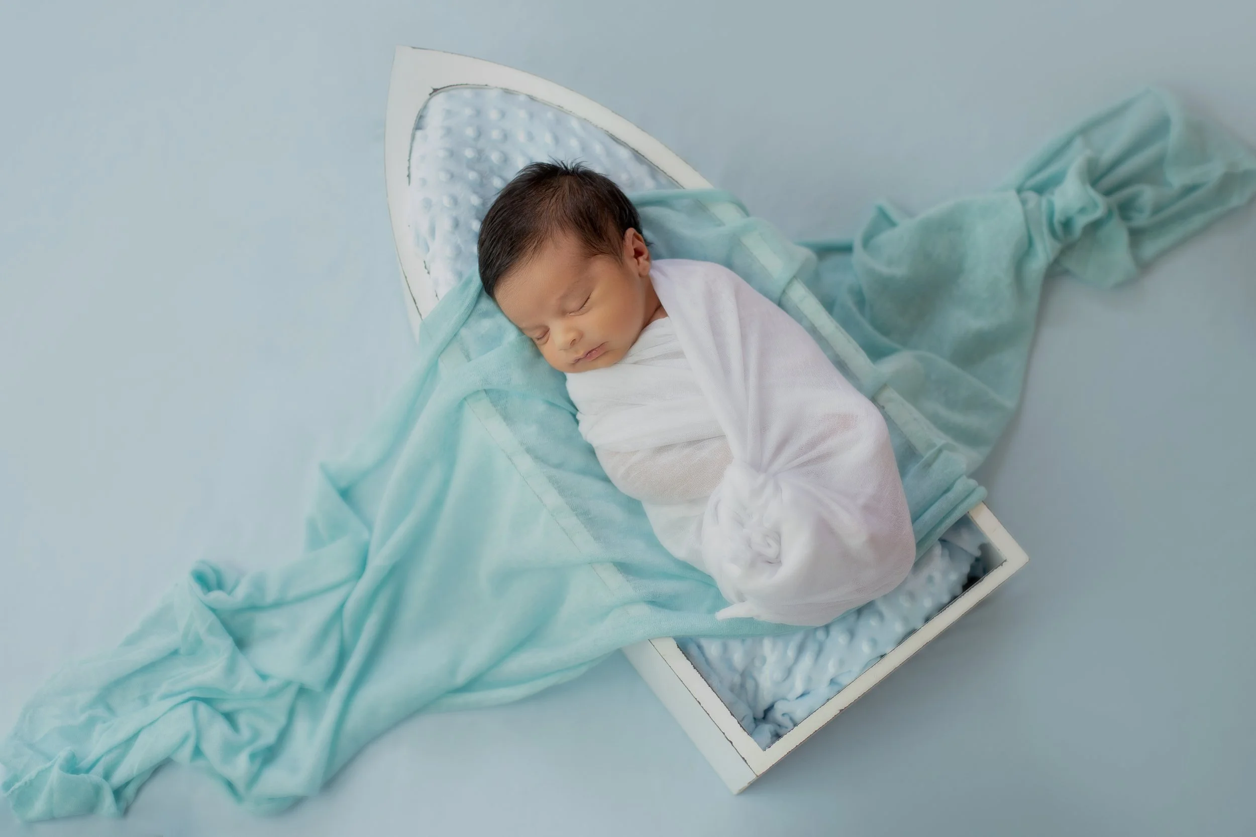 Newborn baby sleeping on a small bed with light blue sheets and a white blanket.