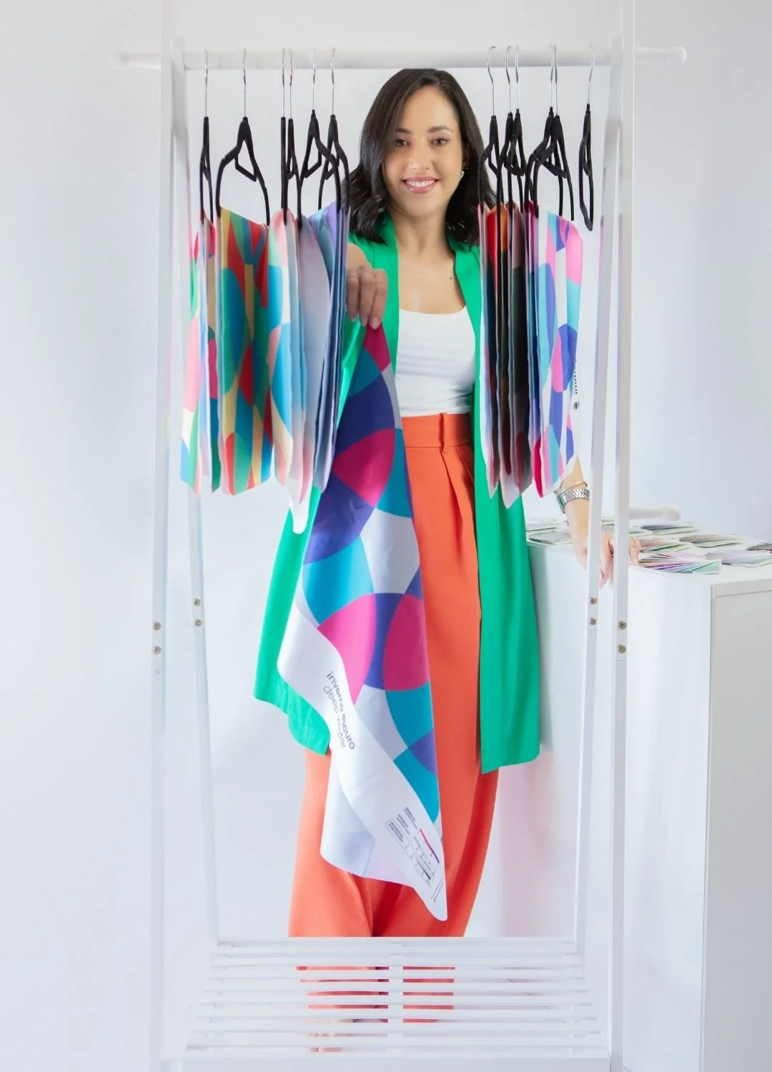 A woman standing behind a white clothing rack with colorful fabric samples hanging from black hangers.
