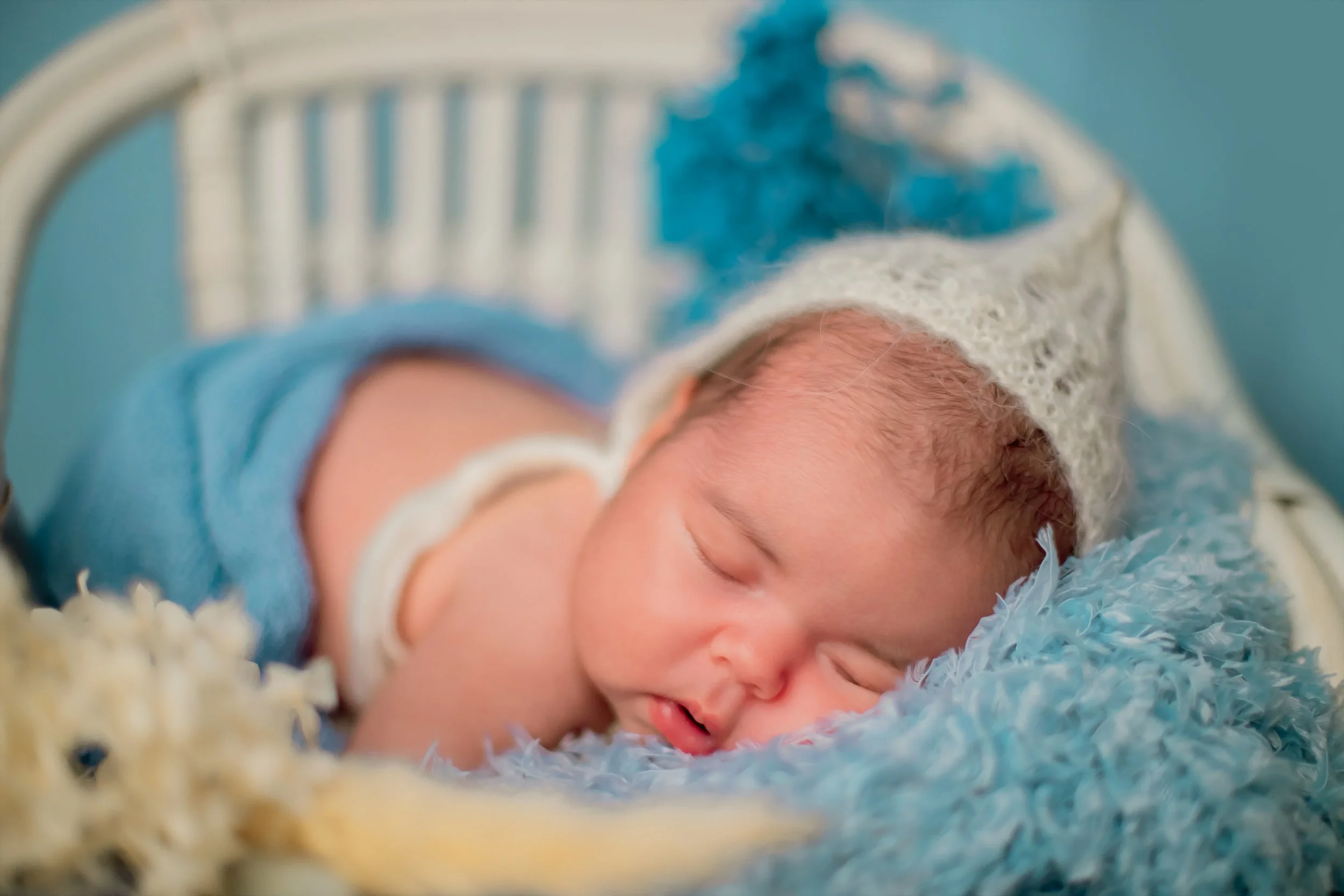 Close-up of a sleeping newborn baby lying on a soft fluffy blanket with a white and blue knitted hat.