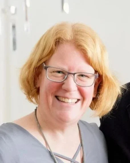 Lächelnde Frau mit Brille und roten Haaren, im Hintergrund eine Tür. Professionelles Porträt in einem Büro. Die Frau heißt Tanja Brammen.