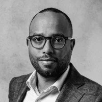 Portrait of a man with glasses, wearing a suit and tie, against a plain background.