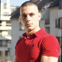 Young man with short hair wearing a red polo shirt outdoors, urban background.