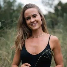 A young woman with long wavy hair smiling outdoors wearing a black spaghetti strap top