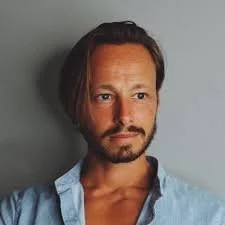 Young man with glasses and a slight smile, black background.