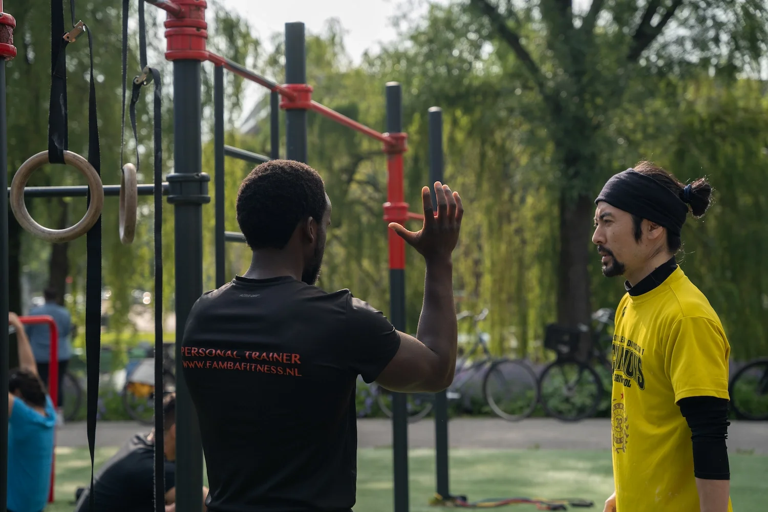 a personal trainers trains his client in calisthenics in a park in amsterdam west