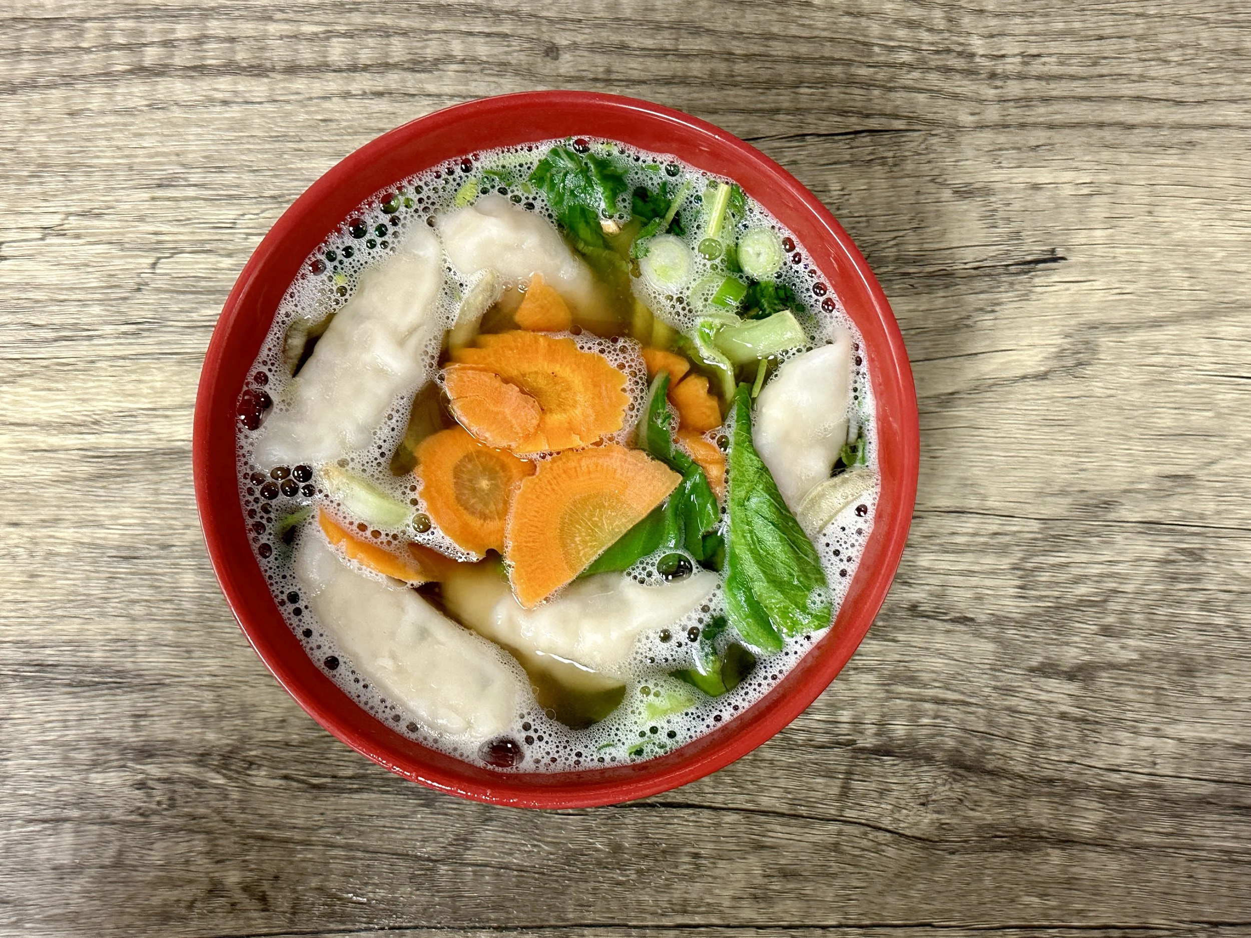Bowl of vegetable soup with carrots, green onions, and leafy greens on a wooden surface.