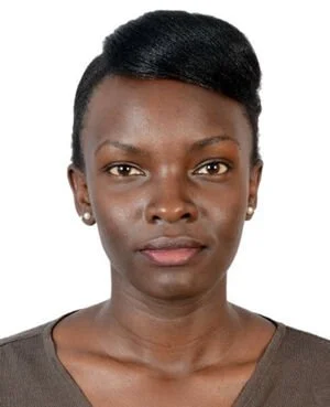 Close-up of a woman with dark skin, short black hair, wearing a dark brown top, against a white background.