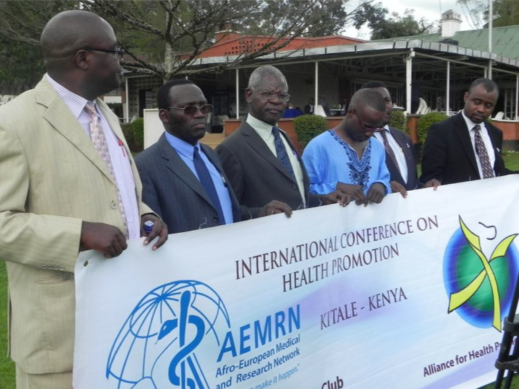 Six men in formal attire holding a banner at an outdoor event promoting health, with a building and trees in the background.