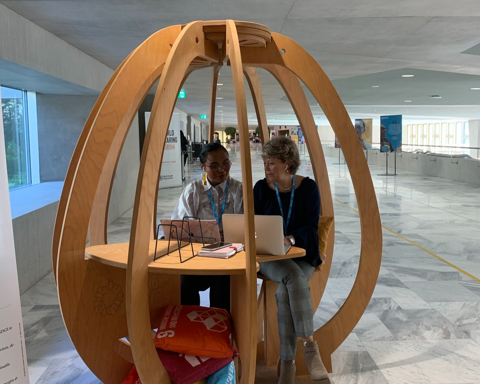 Two women working on laptops inside a wooden structure at a conference or event.