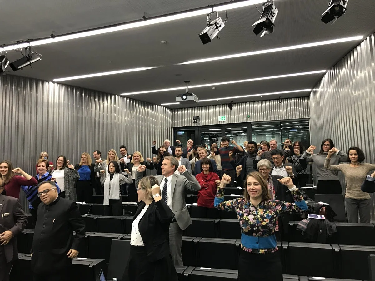 A group of diverse people in a conference room, raising their fists in a celebratory or empowering gesture.